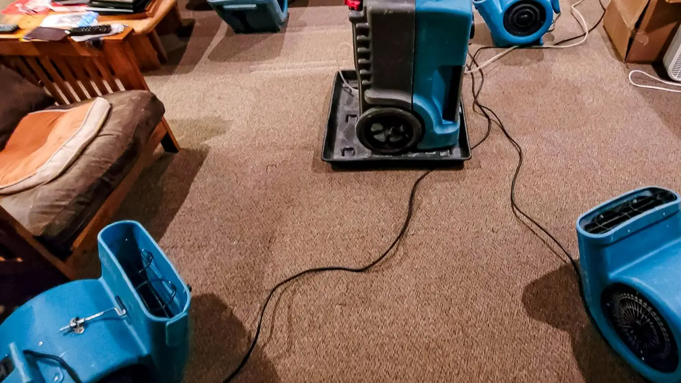 Dehumidifier and air mover drying a carpeted room after water damage