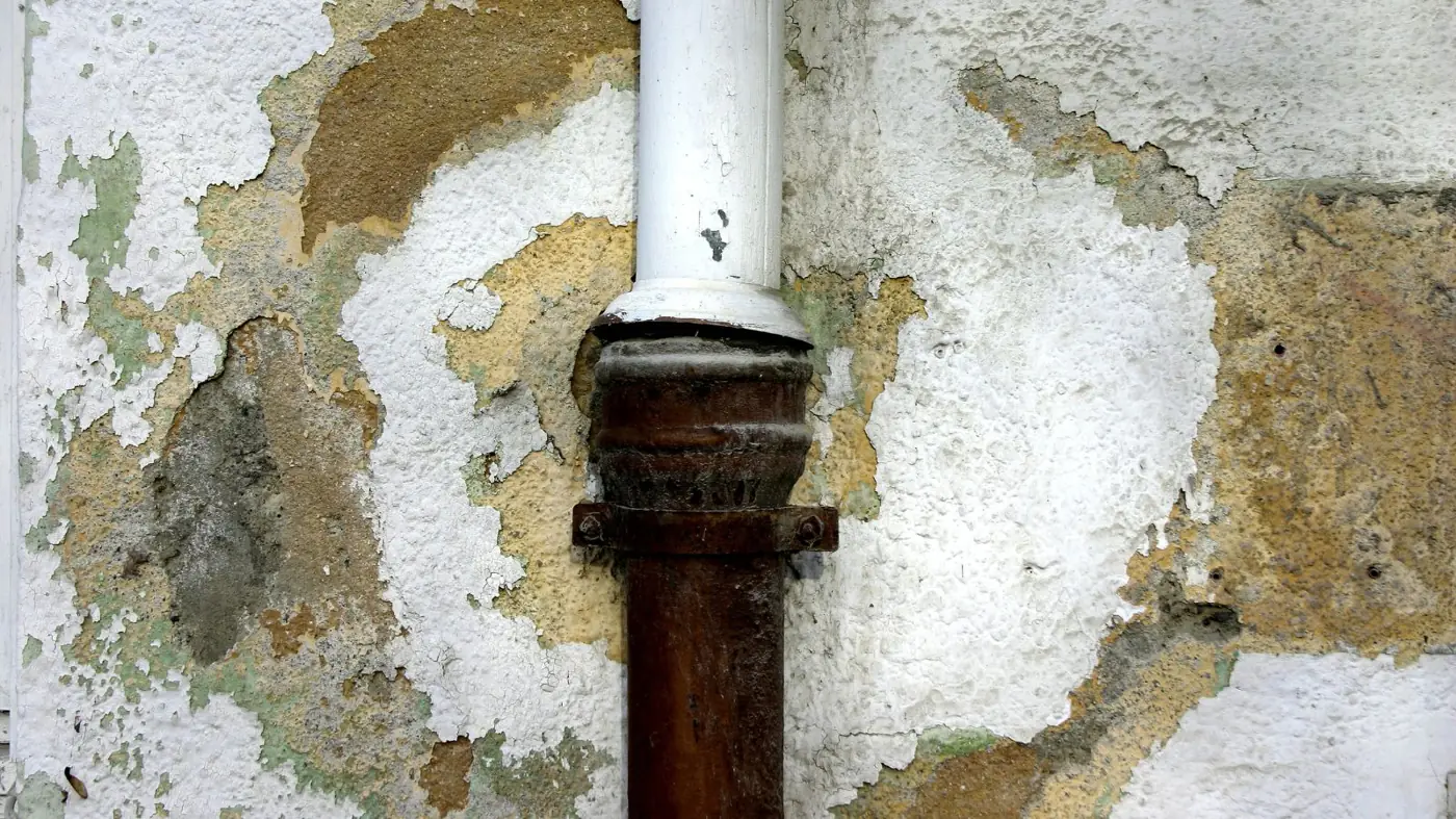 Wall damaged by water around a pipe with peeling paint and plaster